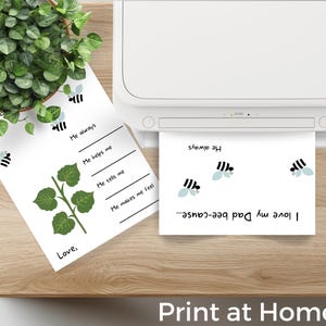 Puede incluir: Una impresora imprime una hoja de papel blanca con el texto "I love my Dad bee-cause..." e ilustraciones de abejas. Otra hoja de papel con ilustraciones de abejas y el texto "I love" est&aacute; junto a una planta en maceta. El texto "Print at Home!" est&aacute; en la parte inferior.