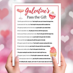 Puede incluir: Una tarjeta de juego imprimible rosa y blanca con el texto "Galentine's Pass the Gift" e instrucciones para un juego de intercambio de regalos. La tarjeta presenta una copa de c&oacute;ctel rosa, una botella de poci&oacute;n roja y una magdalena rosa.