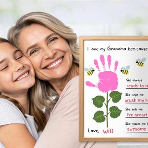 May include: A framed print with the text "I love my Grandma bee-cause..." featuring a pink handprint flower design, bees, and the words "reads to me", "brush my hair", "I'm smart", and "awesome". The print is signed "Love, Will".