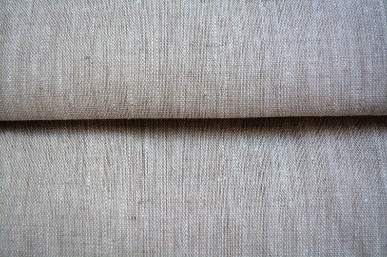 Może przedstawiać: Zbliżenie na złożony kawałek beżowego materiału lnianego o fakturowanym splocie.