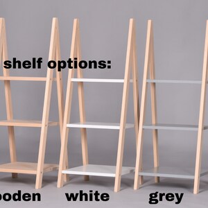 May include: Three wooden A-frame shelves, each with three shelves. The shelves are available in three colors: natural wood, white, and gray. "shelf options:" is written above the shelves.