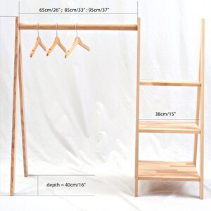 May include: A wooden clothing rack with a shelf unit. The rack is 37 inches tall and 26 inches wide. The shelf unit is 15 inches wide and has three shelves. The rack is made of natural wood and has a rustic look.