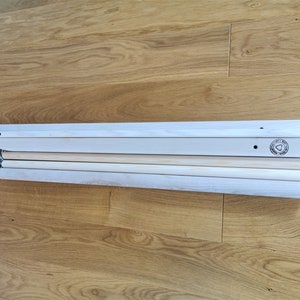 Op de afbeelding: Een set houten pinnen en planken voor het bouwen van een houten schommel. De planken zijn wit en de pinnen zijn van natuurlijke houtkleur. De planken hebben een klein zwart logo aan een uiteinde.