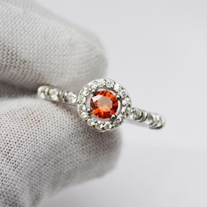 May include: A silver ring with a round orange gemstone surrounded by a halo of smaller white gemstones.