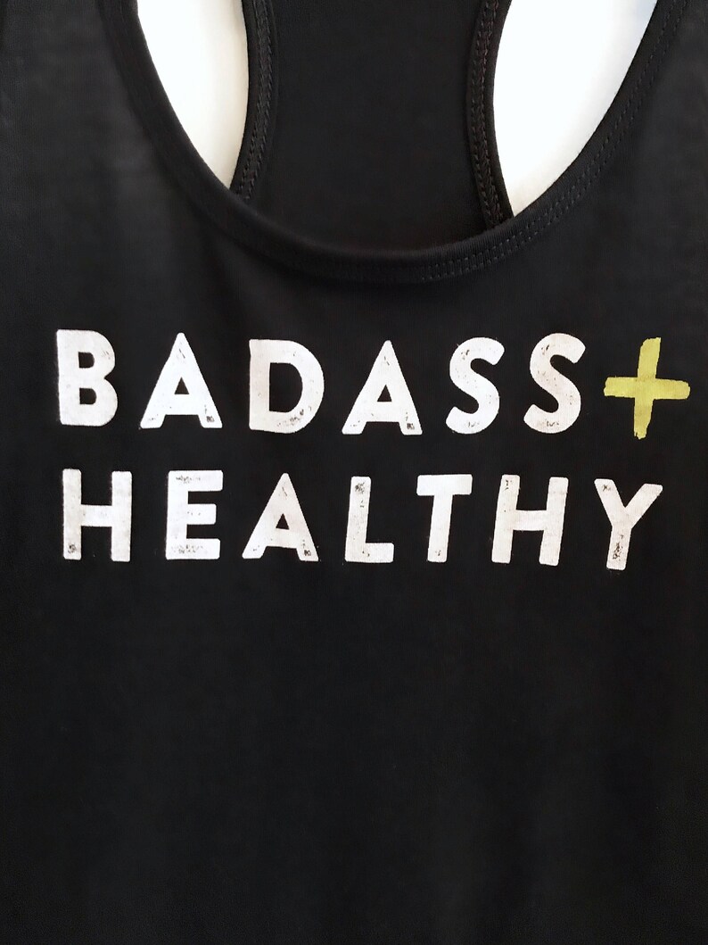 K&ouml;nnte beinhalten: Schwarzes Tanktop mit dem Aufdruck "BADASS+HEALTHY" in Wei&szlig;.