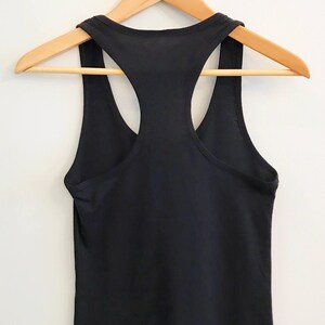 K&ouml;nnte beinhalten: Ein schwarzes Tanktop mit Racerback, das an einem Holzb&uuml;gel h&auml;ngt. Das Tanktop ist schlicht und hat kein sichtbares Design.