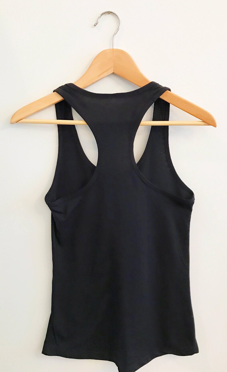 K&ouml;nnte beinhalten: Ein schwarzes Tanktop mit Racerback, das an einem Holzb&uuml;gel h&auml;ngt. Das Tanktop ist schlicht und hat kein sichtbares Design.