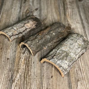 May include: Three pieces of natural bark, each curved into a half-circle shape. The bark is a light brown color with a rough texture.