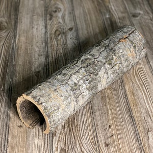 May include: A hollow log made of natural wood with a rough bark texture. The log is lying on a wooden surface.