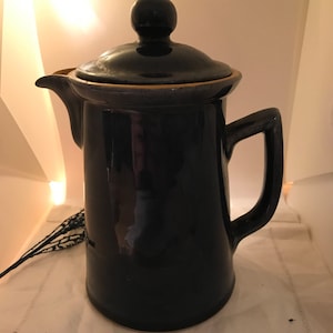 May include: A dark blue ceramic coffee pot with a lid and handle. The pot has a spout and a round knob on top of the lid. The pot is sitting on a white cloth.