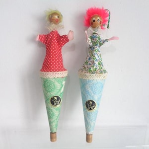 May include: Two vintage handmade clown puppets. One puppet has a red polka-dot dress, the other a floral dress. Both have cone-shaped bodies with a green and blue floral pattern, and wooden heads with yarn hair. Each has a small label.