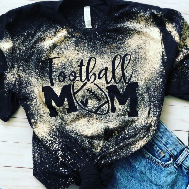 May include: Black t-shirt with a bleach-splattered design. The shirt has the text "Football Mom" in black with a football graphic.