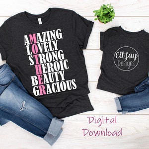 May include: Two dark grey t-shirts with white text. The larger shirt says "AMAZING LOVELY STRONG HEROIC BEAUTY GRACIOUS" with the word "MOTHER" in pink. The smaller shirt says "EllJay Designs" in a circle.