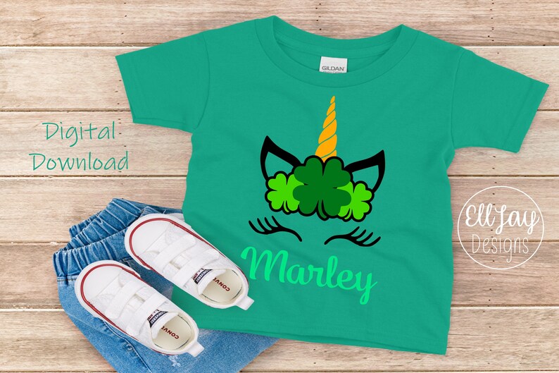 May include: A green t-shirt with a unicorn face design featuring a gold horn and shamrock leaves. The name "Marley" is written in green below the unicorn face.