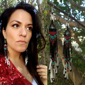 May include: A pair of long, beaded earrings with a turquoise, red, and black geometric pattern. The earrings are made with white shell beads and have a silver turtle charm at the top.