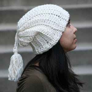 May include: A white crocheted beanie with a long tassel. The beanie is slouchy and has a unique design.