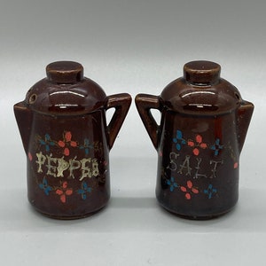 May include: A set of brown ceramic salt and pepper shakers with a floral design and the words "SALT" and "PEPPER" written on them.
