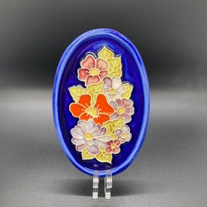 Può includere: Un piatto ovale in ceramica blu con un design floreale in rilievo. I fiori sono in tonalità di rosso, giallo, rosa e bianco.