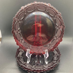 Op de afbeelding: Set van vier rode glazen dessertborden met een gegolfde rand en een reliëfdesign. De borden zijn op elkaar gestapeld.