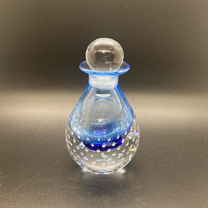 May include: A clear glass bottle with a blue and white design. The bottle has a round, clear glass stopper and a textured, bubbled surface.