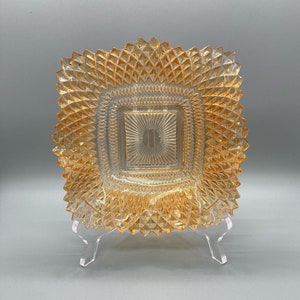 Puede incluir: Un plato cuadrado de vidrio ámbar con un patrón de diamante. El plato tiene una sección central elevada con un patrón de sol.