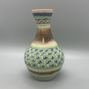 May include: A ceramic vase with a rounded body and a slender neck. The vase is decorated with a pattern of brown, green, and blue. The body has a repeating pattern of blue and yellow shapes on a green background. The neck has a geometric design.
