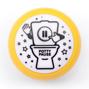 May include: A round yellow button with a white center featuring a black line drawing of a toilet with arms. The toilet has a pause symbol on the tank and the text POTTY PAUSE printed on the bowl, surrounded by small black stars on the white background.