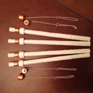 May include: Five white cotton wicks with copper caps and silver chains. The wicks are arranged in a row, with the chains hanging down from the caps.