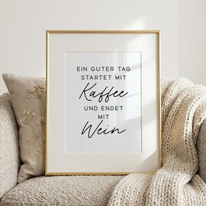 May include: A framed print with a gold-colored frame. The white print features black script that reads, "EIN GUTER TAG STARTET MIT Kaffee UND ENDET MIT Wein."