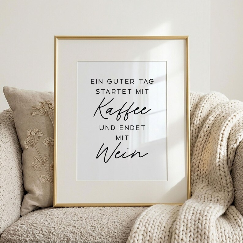 May include: A framed print with a gold-colored frame. The white print features black script that reads, "EIN GUTER TAG STARTET MIT Kaffee UND ENDET MIT Wein."