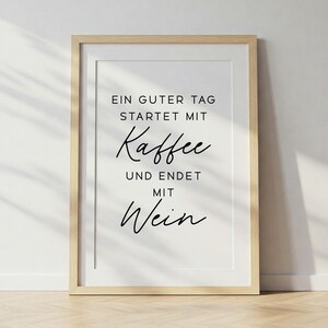 May include: A framed print with the text "EIN GUTER TAG STARTET MIT Kaffee UND ENDET MIT Wein" in black script. The print is in a light wood frame and is displayed against a white wall.