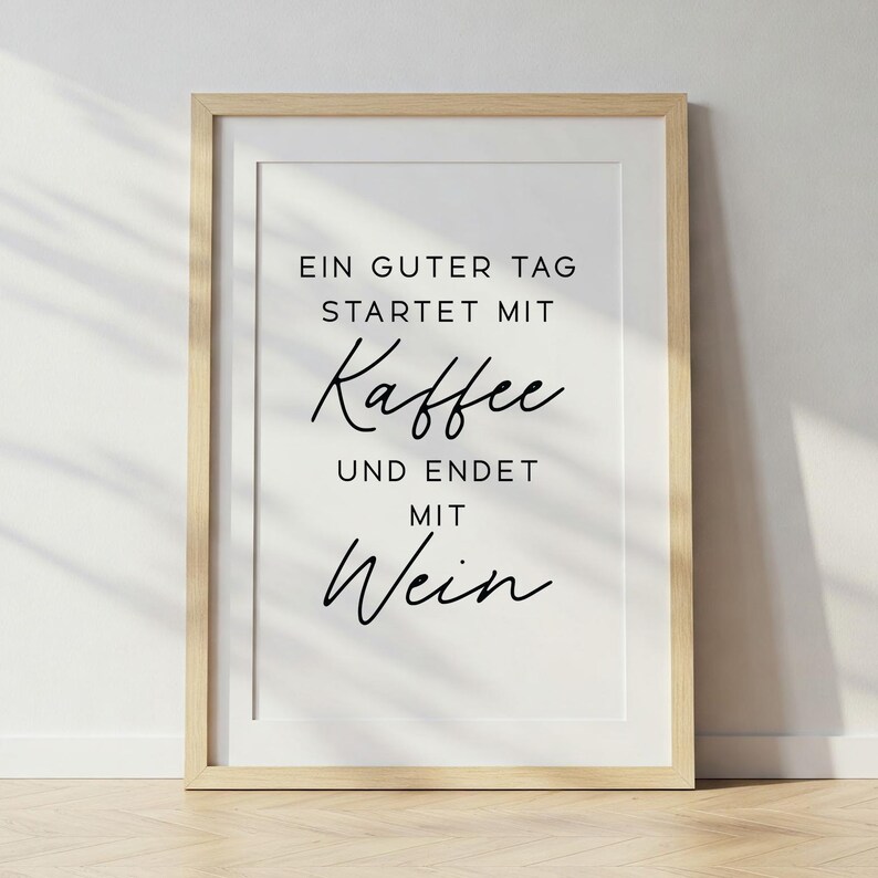 May include: A framed print with the text "EIN GUTER TAG STARTET MIT Kaffee UND ENDET MIT Wein" in black script. The print is in a light wood frame and is displayed against a white wall.