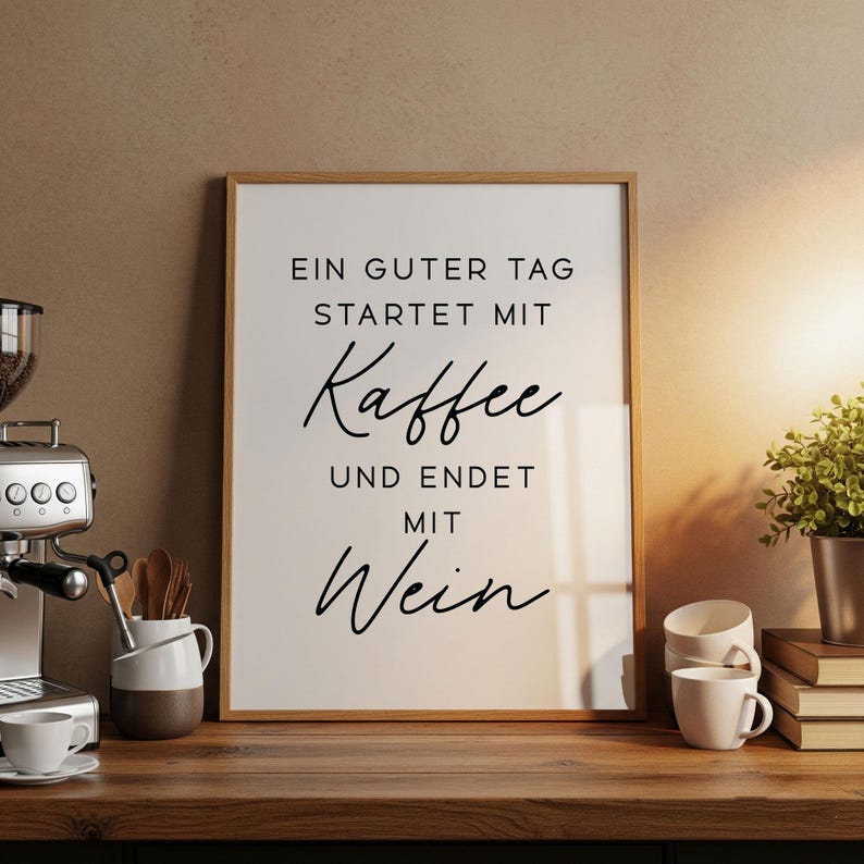 May include: A framed print with the text "EIN GUTER TAG STARTET MIT Kaffee UND ENDET MIT Wein" in black script. The print is in a light wood frame and sits on a wooden surface, alongside a coffee machine, cups, and a small plant.