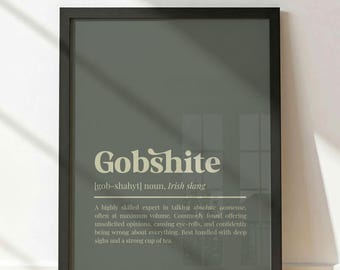 Può includere: Una stampa da parete incorniciata con una definizione da dizionario della parola Gobshite. Il testo è color crema su uno sfondo verde oliva tenue, definendo il sostantivo come un esperto nel dire assurdità a volume alto.