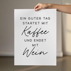 May include: A white poster with black text. The text reads, "EIN GUTER TAG STARTET MIT Kaffee UND ENDET MIT Wein." The poster is held by a hand.