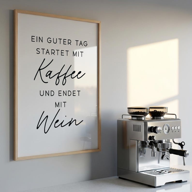 May include: A framed print with the text "EIN GUTER TAG STARTET MIT Kaffee UND ENDET MIT Wein" hangs next to a stainless steel espresso machine. The machine has a portafilter and two glass containers on top.
