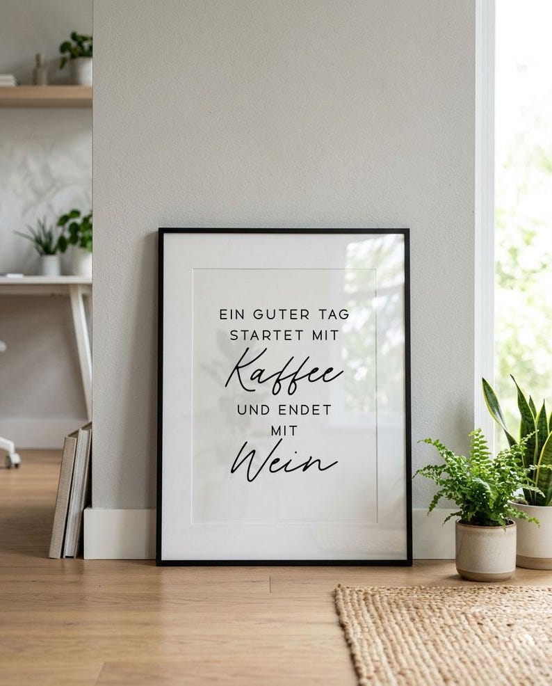 May include: Framed print with the text "EIN GUTER TAG STARTET MIT Kaffee UND ENDET MIT Wein" in black script on a white background. The frame is black. The print is displayed on a wooden floor.