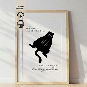 Peut inclure: Une affiche encadrée avec une illustration de chat noir et le texte "please close the lid" et "the cat has a drinking problem." Le produit numérique est encadré de bois clair et a un fond blanc, idéal pour la décoration.