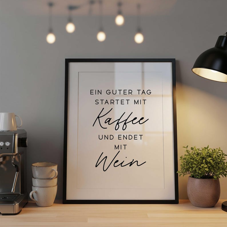 May include: Framed print with black text that reads "Ein guter Tag startet mit Kaffee und endet mit Wein." A coffee machine, stacked mugs, and a potted plant are on a wooden surface. A black desk lamp and hanging lights are also visible.