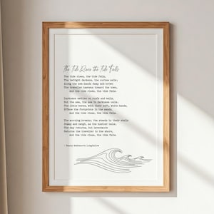 Puede incluir: Una impresión enmarcada con el poema "The Tide Rises, The Tide Falls" de Henry Wadsworth Longfellow. El texto está en negro, con una fuente elegante sobre un fondo blanco, con un dibujo lineal de olas en la parte inferior. El marco es de color marrón claro.