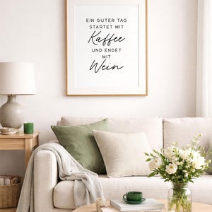 May include: A living room scene with a framed print reading "Ein guter Tag startet mit Kaffee und endet mit Wein." A beige sofa is adorned with green and cream pillows, a blanket, and a wooden coffee table with a vase of flowers.