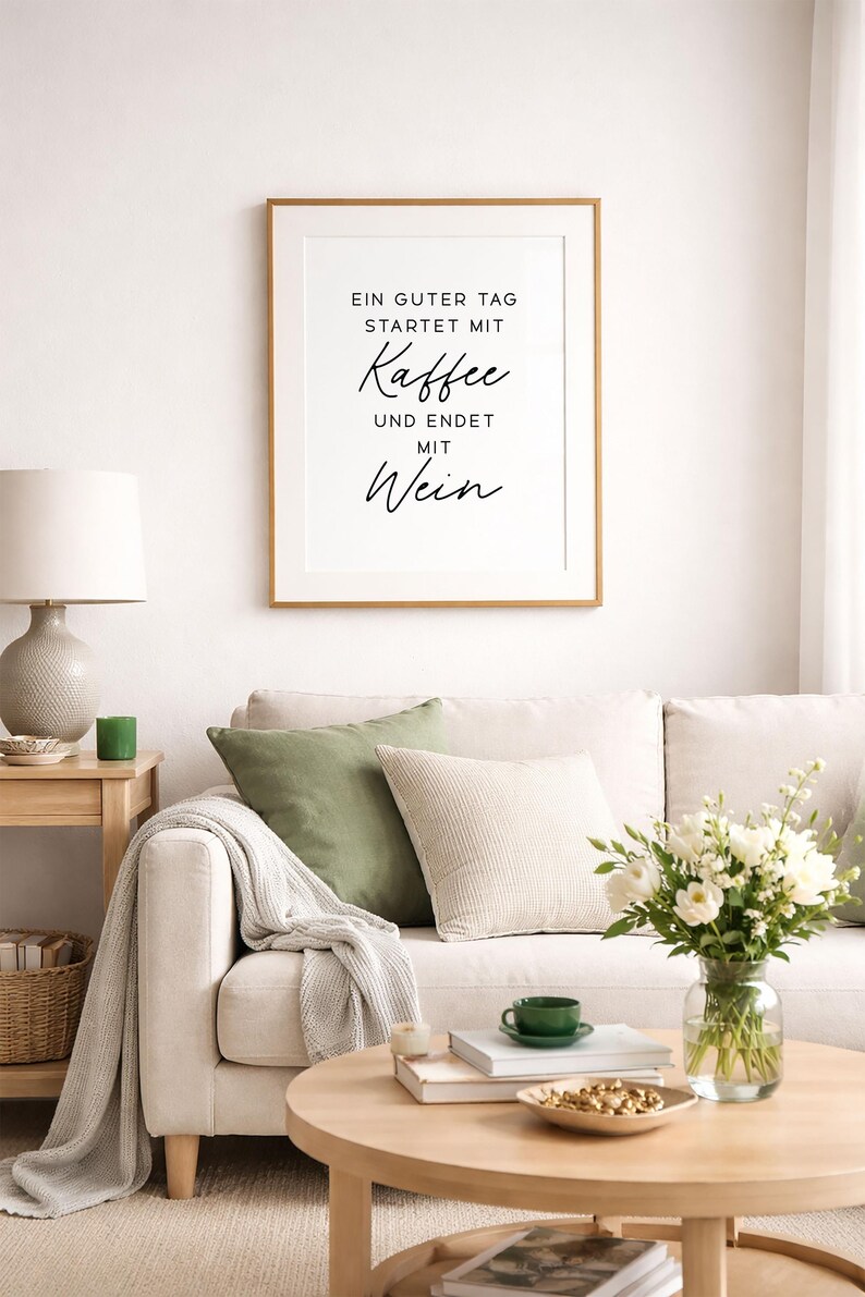 May include: A living room scene with a framed print reading "Ein guter Tag startet mit Kaffee und endet mit Wein." A beige sofa is adorned with green and cream pillows, a blanket, and a wooden coffee table with a vase of flowers.