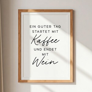 May include: Framed print with the text "EIN GUTER TAG STARTET MIT Kaffee UND ENDET MIT Wein" in black script on a white background. The frame is a light brown wood.