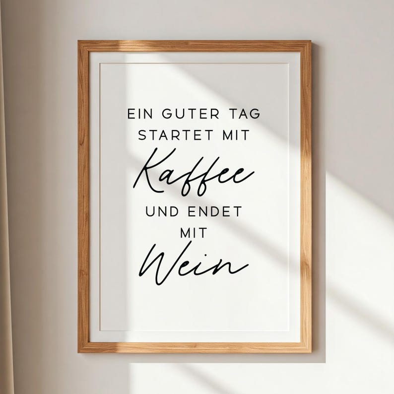 May include: Framed print with the text "EIN GUTER TAG STARTET MIT Kaffee UND ENDET MIT Wein" in black script on a white background. The frame is a light brown wood.