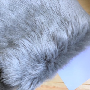 May include: A soft, gray faux fur throw pillow. The pillow is made of a fluffy, plush material that is perfect for adding a touch of luxury to any room.