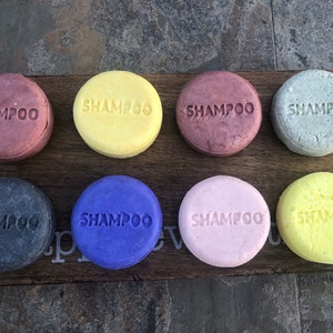 May include: Eight round shampoo bars in different colors, including pink, purple, yellow, gray, and black. Each bar has the word "SHAMPOO" embossed on the top.
