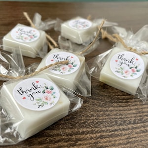 May include: Five small white square soaps wrapped in clear cellophane bags tied with twine. Each soap has a round sticker with a floral design and the text "thank you".