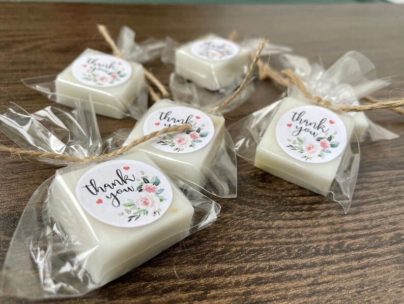 May include: Five small white square soaps wrapped in clear cellophane bags tied with twine. Each soap has a round sticker with a floral design and the text "thank you".