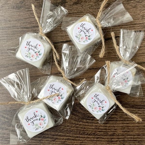 May include: Six small white square soaps wrapped in clear cellophane bags tied with twine. Each soap has a round sticker with the text "Thank you" and a floral design.