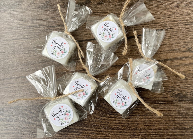 May include: Six small white square soaps wrapped in clear cellophane bags tied with twine. Each soap has a round sticker with the text "Thank you" and a floral design.